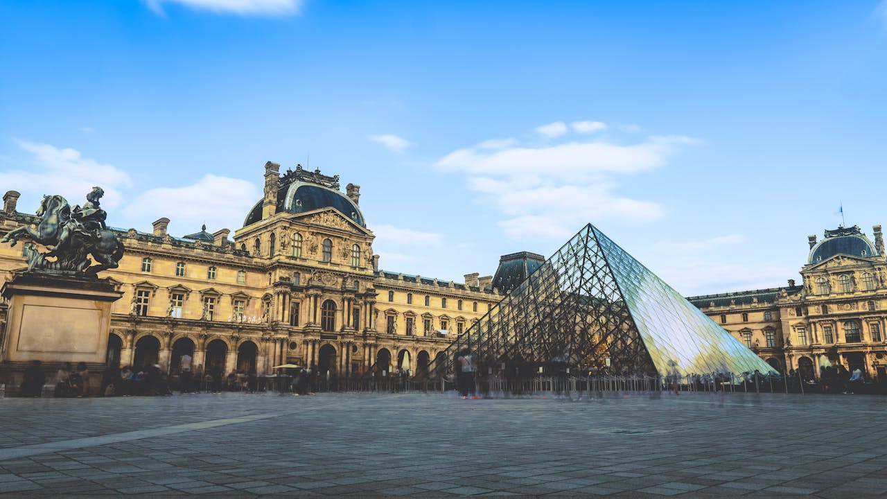 The iconic glass pyramid of the Louvre Museum against a clear blue sky in Paris.