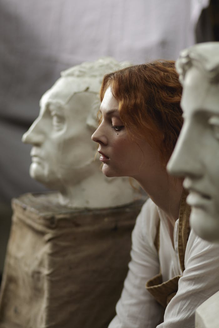 Pensive woman sitting with classical sculptures, reflecting beauty and art.